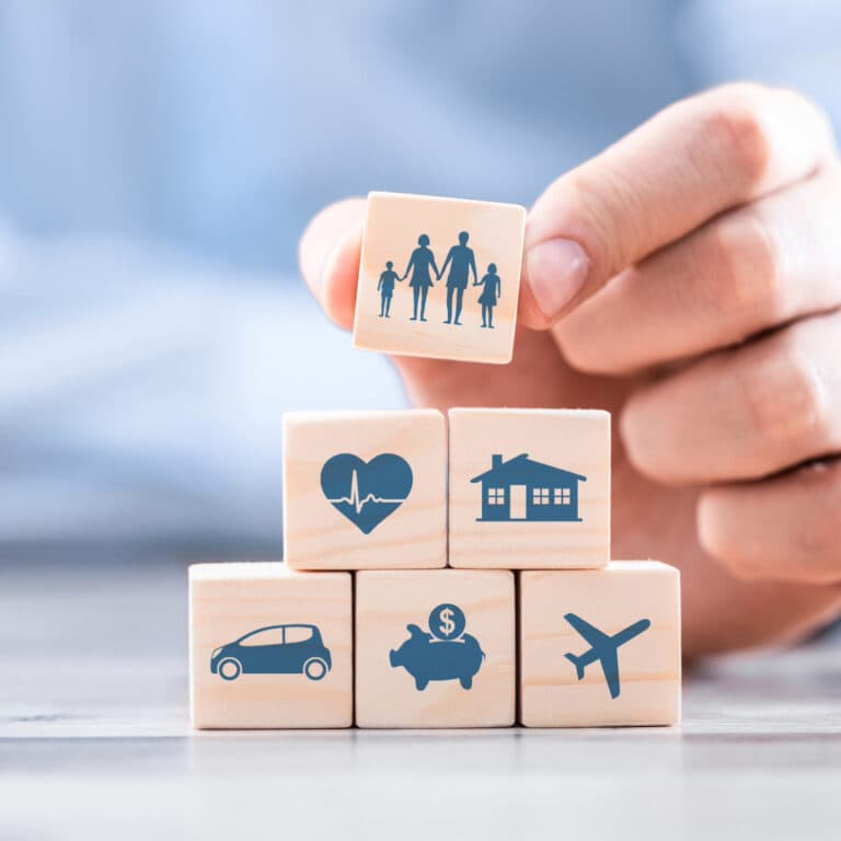 Hand arranging wooden blocks with icons representing family, health, home, car, money, and travel